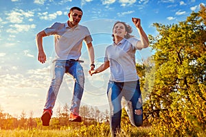 Young man and woman running and jumping. Couple having fun in spring field at sunset. Guys laughing