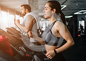 Young man and woman are running on the running machine. They do this exercise every time they come to fitness club.Close