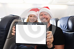 Young man and woman in santa claus hats holding digital tablet in cabin of airplane