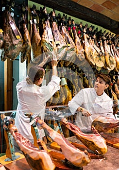 Young man and woman selling spanish jamon at counter