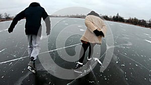 Young man and woman shod in figure skates sliding on ice rink outdoor. Friends learning to skate on frozen river at