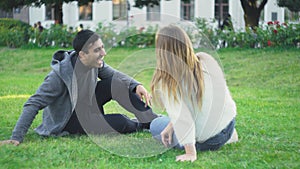 Young man and woman sit on grass in park and laugh. Media. Beautiful couple relax and laugh sitting on green grass