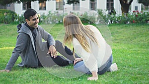 Young man and woman sit on grass in park and laugh. Media. Beautiful couple relax and laugh sitting on green grass