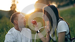 A young man and woman are sitting on a green meadow and eating an apple. Romance, love