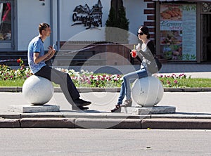 Young man and young woman sitting on large stone balls mounted on the street