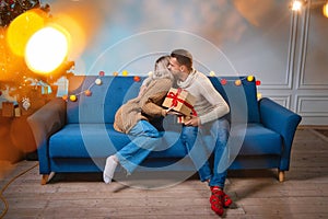 A young man and a woman are sitting on a sofa and exchanging gift boxes in beautiful wrapping paper in the New Year