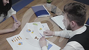 Young man and woman sitting at the table in the office. Colleagues discussing charts and schemas depicted on paper. Co