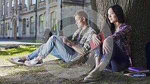 Young man and woman sitting under tree, being shy at first meeting, awkwardness