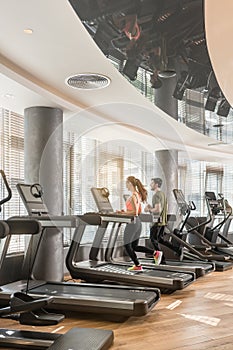 Young man and woman smiling while running side by side on treadmills