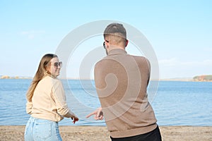 Young man and woman in sunglasses, sweater and jeans are having fun and dancing on the beach.