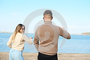 Young man and woman in sunglasses, sweater and jeans are having fun and dancing on the beach.