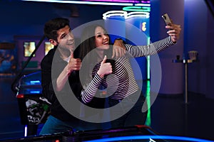 Young man and woman taking selfie on cellphone while playing air hockey