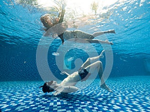 Young man and woman underwater view in the pristine blue swimming pool.