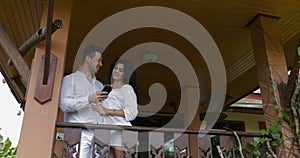 Young man and woman use cell smart phone on balcony in hotel, happy smiling couple embracing surfing internet together