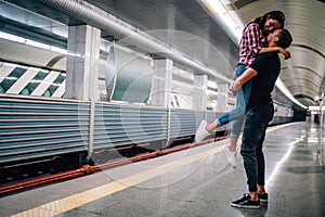 Young man and woman use underground. Couple in subway. Cheerful picture of young man holding woman in hands. She smile