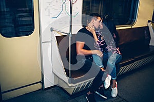 Young man and woman use underground. Couple in subway. Kissing scene on bench in metro carriage. Embrace and cheerful