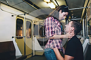 Young man and woman use underground. Couple in subway. She stand upon him and embrace. Guy look at her and smile. Love