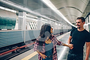 Young man and woman use underground. Couple in subway. Young man follow woman and hold her hand. They look at each other