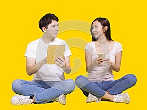 Young man and woman using tablet computer and smartphone.Isolated on yellow background