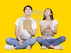 Young man and woman using tablet computer and smartphone.Isolated on yellow background.Look above