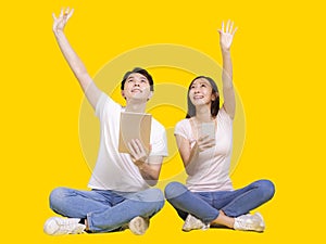 Young man and woman using tablet computer and smartphone.Isolated on yellow background.Raising hands