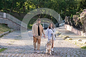 Young man and woman walking with gorgeous australian collie in urban area.