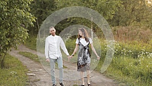 Young man and woman walking in a green meadow in the park holding hands in the summer. Romance, love, relationship