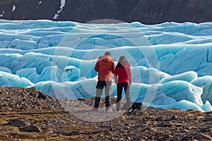 Young Man and woman watching and navigating a flying drone in blue clear Sky before of beautiful evening scenery of Skaftafell