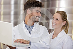 young man and woman wearing labcoats looking at laptop