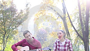 Young man and women playing guitar and singing in park