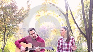 Young man and women playing guitar and singing in park