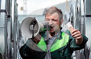 A young man in work clothes shouts loudly into a loudspeaker inviting to join him at work. The man holds out banknotes as a