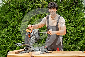 Young man in a work uniform repairs a miter saw using a screwdriver