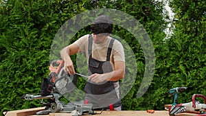 Young man in a work uniform repairs a miter saw using a screwdriver