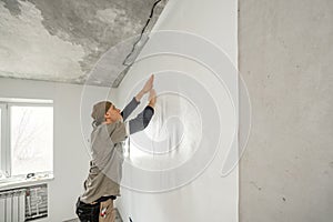 Young man, worker glueing wallpapers on concrete wall. Repair the apartment. Home renovation concept. White Wallpaper