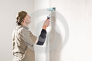 Young man, worker glueing wallpapers on concrete wall. Repair the apartment. Home renovation concept. White Wallpaper