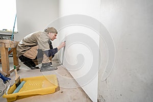 Young man, worker glueing wallpapers on concrete wall. Repair the apartment. Home renovation concept. White Wallpaper
