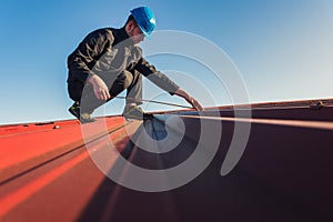 Young man worker in helmet holding meter tape on roof with blue sky. Roofer work background