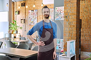 Young man worker, owner in apron looking at camera in restaurant, coffee shop