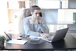 A young man working at a desk with a laptop.