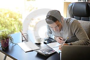 A young man working at a desk with a laptop.