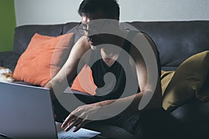 Young man working on his laptop while sitting on a sofa at home