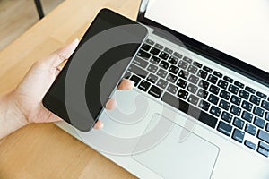 Young man working from home using smart phone mockup and laptop computer, man`s hands using smart phone in interior.