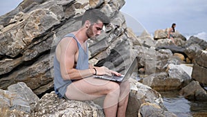 Young man working on laptop computer at beach