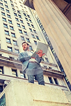 Young man working on laptop computer outside office building in New York City