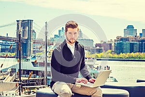 Young Man working on laptop computer by river in New York City