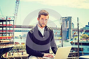 Young Man working on laptop computer by river in New York City