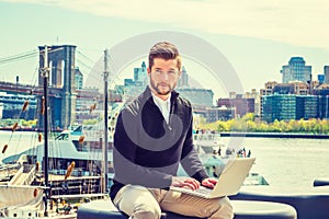 Young Man working on laptop computer by river in New York City