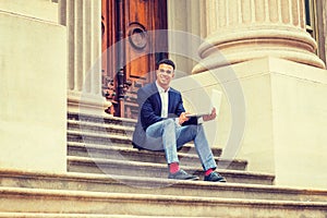 Young man working on laptop computer, sitting on stairs  outside office building in New York City