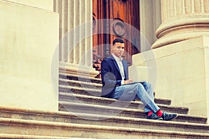 Young man working on laptop computer, sitting on stairs  outside office building in New York City